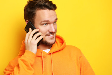 Happy young man talking on cell phone over yellow  background