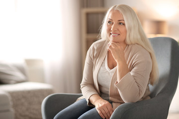 Portrait of beautiful mature woman sitting in armchair at home