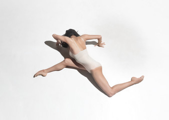 Young beautiful dancer in beige dress dancing on gray background