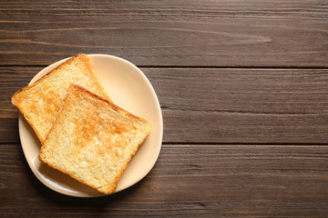 Plate with toasted bread on wooden background