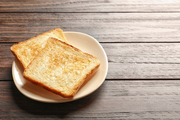 Plate with toasted bread on wooden background