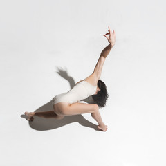 Obraz premium Young beautiful dancer in beige dress dancing on gray background