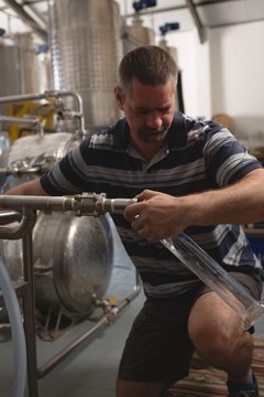 Male worker filling gin in measuring cylinder from distillery