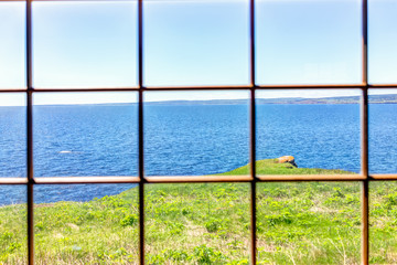 Looking through old window of house with cliff and ocean view in Bonaventure Island, Quebec, Canada