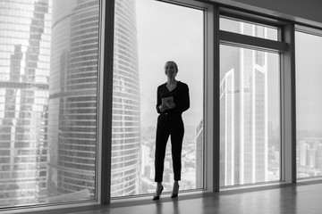 Fototapeta na wymiar Business woman holding a tablet and standing in a modern office. Panoramic windows background.
