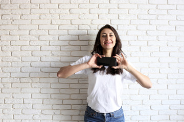 Happy millennial girl having fun indoors. Portrait of young woman with diastema gap between teeth. Beautiful smile. Minimalistic interior, white brick textured wall background, loft style. Copy space.