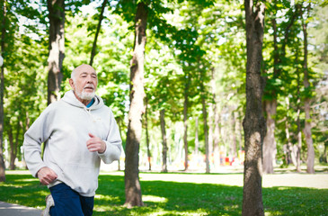 Fototapeta premium Elderly man running in green park, copy space