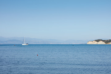 Fototapeta na wymiar Fantastic seaside view at the sea with the alone yacht on the horizon, Corfu island, Greece. Sunny day, minimalism, calm and silence.