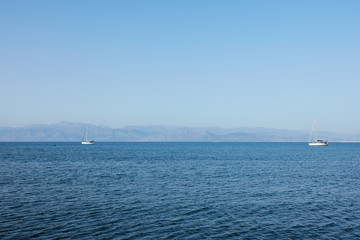 Obraz premium Fantastic seaside view at the sea with the two yachts on the horizon, Corfu island, Greece. Sunny day, minimalism, calm and silence.