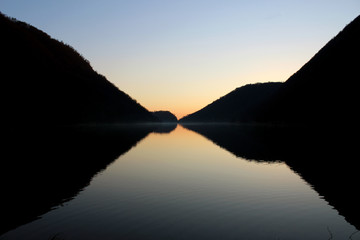 Obraz premium Perfect symmetrical reflection of mountain silhouette on a flat lake surface at dusk
