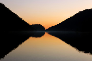 Perfect symmetrical reflection of mountain silhouette on a flat lake surface at dusk