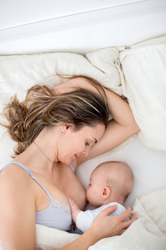 Young mother breastfeeds her baby, holding him in her arms and smiling