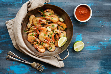 Shrimp fried in a frying pan with garlic and spices. Blue wooden nautical background
