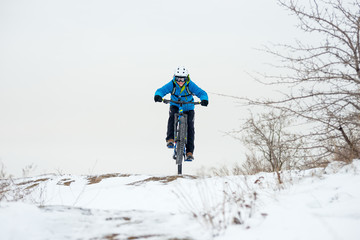 Cyclist in Blue Riding Mountain Bike on Rocky Winter Hill Covered with Snow. Extreme Sport and Enduro Biking Concept.