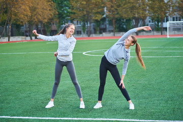 Two beautiful sports girls exercising together on a lawn