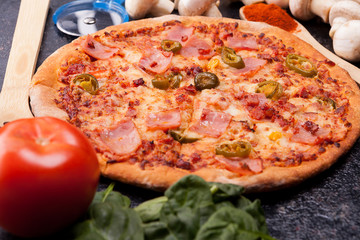 Close up of pizza surrounded with ingredients which it is made from on dark wooden table