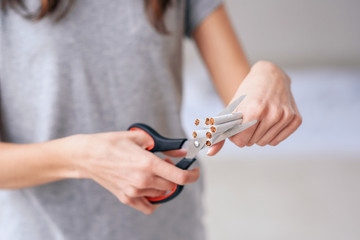 Concept of health protection. Quit smoking, health care concept. No smoking. Close up of female hands holding bunch of cigarettes and cutting them in halves with ccissors. Stop smoking concept.