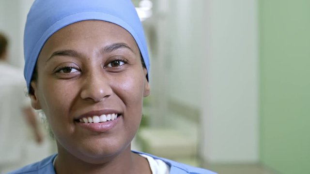 PAN With Close Up Of Happy Female Nurse In Blue Scrubs And Cap Smiling Before Camera