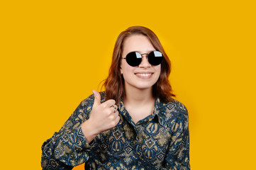 Photo of excited happy young woman standing isolated over yellow background and showing thumbs up gesture. Looking camera.