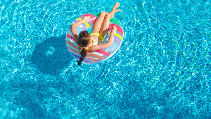 Aerial top view of little girl in swimming pool from above, kid swims on inflatable ring donut , child has fun in water on family vacation resort
