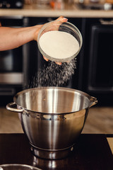 Female hand pour sugar into a big metal bowl for making a dough. Home cooking on kitchen.