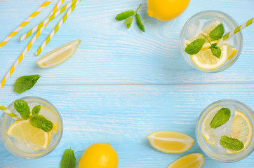 Cold refreshing summer drink with lemon and mint on light blue wooden background, top view, flat lay, copy space.