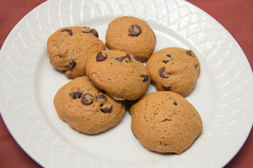Table with chocolate chips cookies, book, cup of coofee, camera and hat