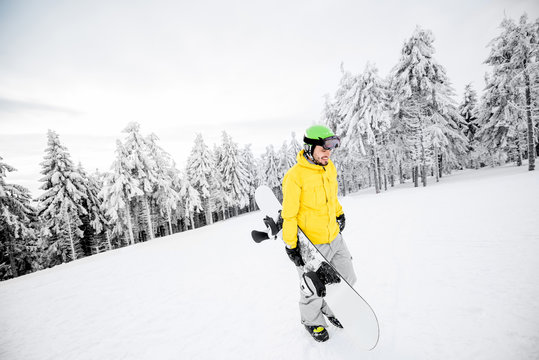 Man in yellow winter clothes walking with snowboard at the snowy mountains
