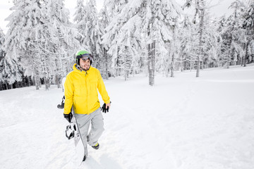 Fototapeta na wymiar Man in yellow winter clothes walking with snowboard at the snowy mountains