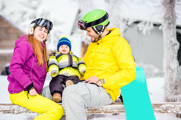 Happy family with baby boy in winter spots clothes sitting on the bench outdoors during the winter vacations