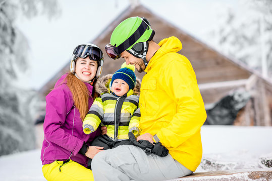 Happy family with baby boy in winter spots clothes sitting on the bench outdoors during the winter vacations