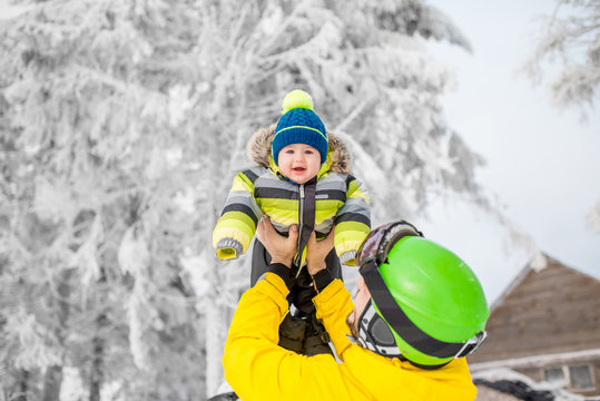 Happy father playing with baby boy standing in winter spots clothes outdoors during the winter vacations