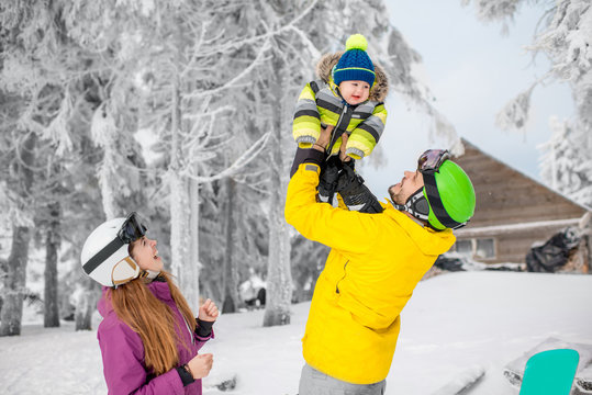 Happy family playing with baby boy standing in winter spots clothes outdoors during the winter vacations