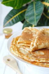 Thin russian pancakes on a plate on white wooden table. Shrovetide. Healthy breakfast concept. Close up.