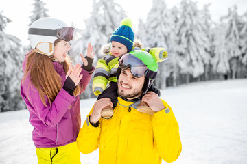 Portrait of a happy family playing with baby boy during the winter vacations on the beautiful mountains with snow-covered forest on the background