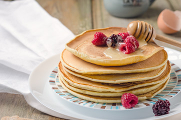 Photo of delicious pancakes with berries and honey over wooden tabe