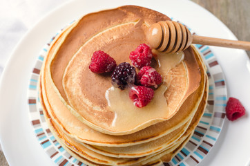 Photo of delicious pancakes with berries and honey over wooden tabe
