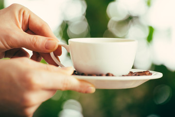 Young wooman hands with cup of coffee on green nature blurred background with bokeh