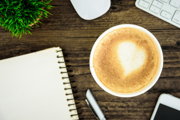 A latte coffee with art heart milk on the brown wood desk table from top view and copy space. Flat lay with desk, business and valentine concept.