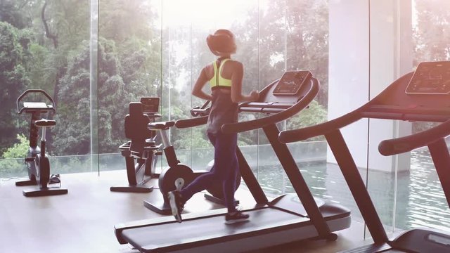 SLOW MOTION. Cute Asian girl on treadmill at gym. Panoramic window, healthy fitness lifestyle concept