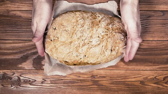 Man puts whole homemade bread on wooden table. Delicious homebaked bread on kraft paper.