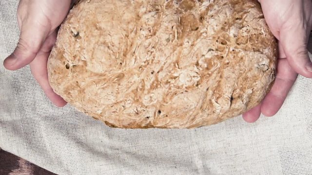Man puts whole homemade bread on wooden table, slow motion. Delicious homebaked bread on linen napkin.