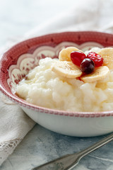 Bowl with milk rice porridge, banana, berries and honey.