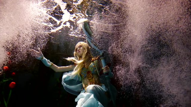 Mysterious woman elf is standing underwater among dozens flowers and bubbles.