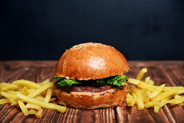 Delicious fresh crispy american burger with beef, herbs, onions and potatoes on a wooden table