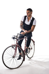 Obraz premium Portrait of young tattooed man in elegant clothes and shoes riding a bicycle. Studio shot. Full body shot