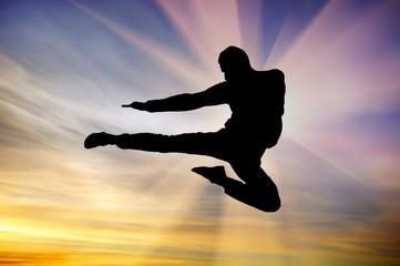 silhouette of a man flying kick in sunset sky background. Martial arts composition.