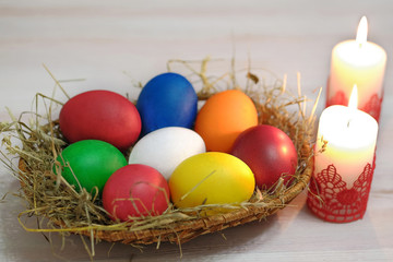 In the wicker basket there are colored Easter eggs and beside it there are two burning candles.