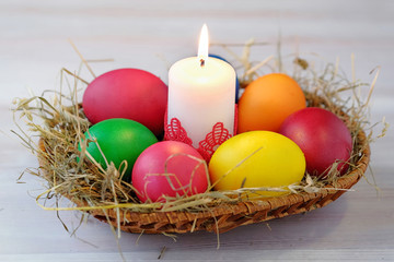 Obraz na płótnie Canvas In the wicker basket lie Easter multi-colored eggs and a burning candle.