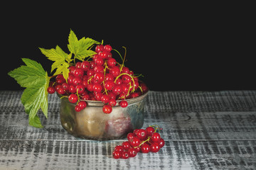 Wooden utensils with ripe red currant berries on a dark background.
